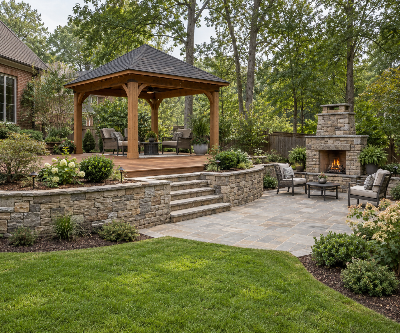 Wooden gazebo on a raised deck with stone retaining walls and steps leading to a patio with an outdoor fireplace.