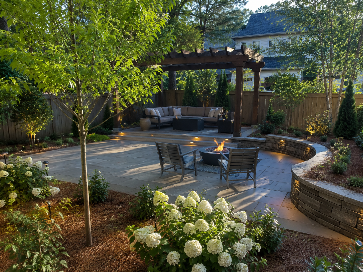 Backyard patio landscape with pergola seating area, fire feature, stone patio, landscape lighting, pine straw, and hydrangeas