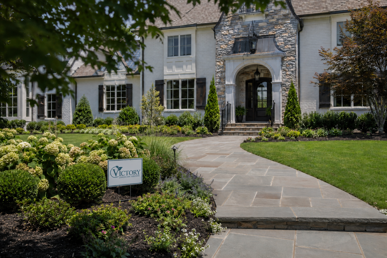 Front yard landscape design with stone walkway, layered planting beds, lawn, and Victory Landscape Services sign